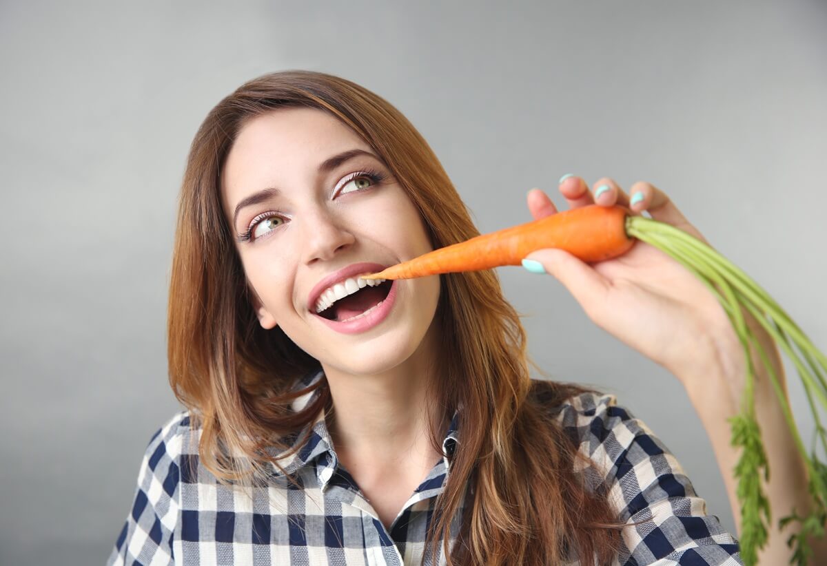Dieta na zdrowe zęby - młoda, uśmiechnięta kobieta gryząca marchewkę