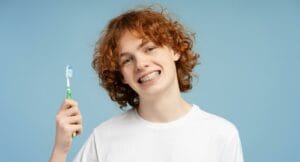 Higiena jamy ustnej z aparatem ortodontycznym - młody człowiek z aparatem ortodontycznym trzymający szczoteczkę do zębów