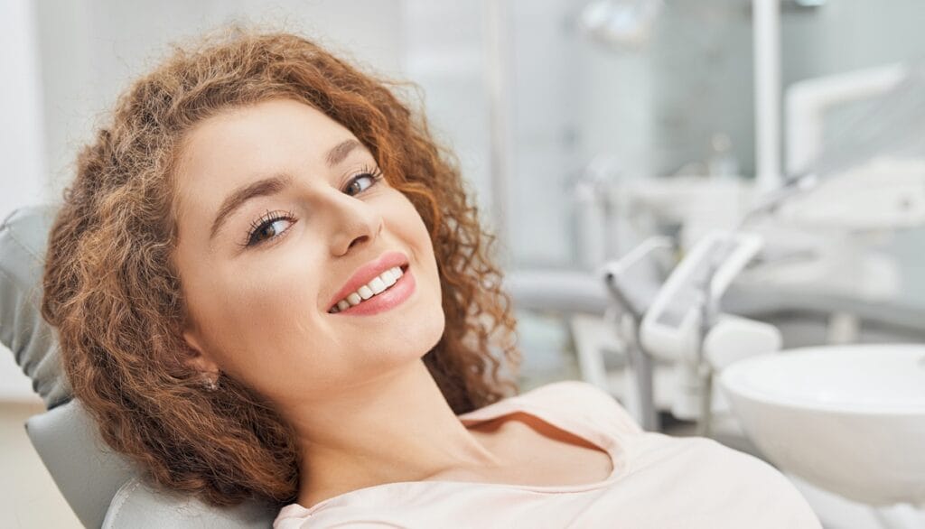 Zabiegi stomatologii estetycznej - uśmiechnięta kobieta na fotelu stomatologicznym